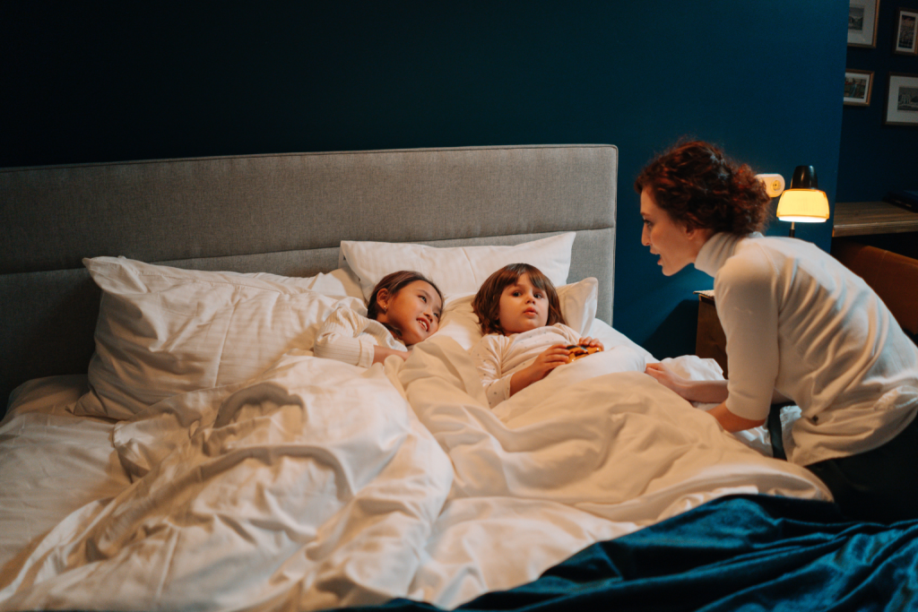 Mother talking calmly to her children in bed as part of a comforting bedtime routine that promotes emotional connection and better sleep.
